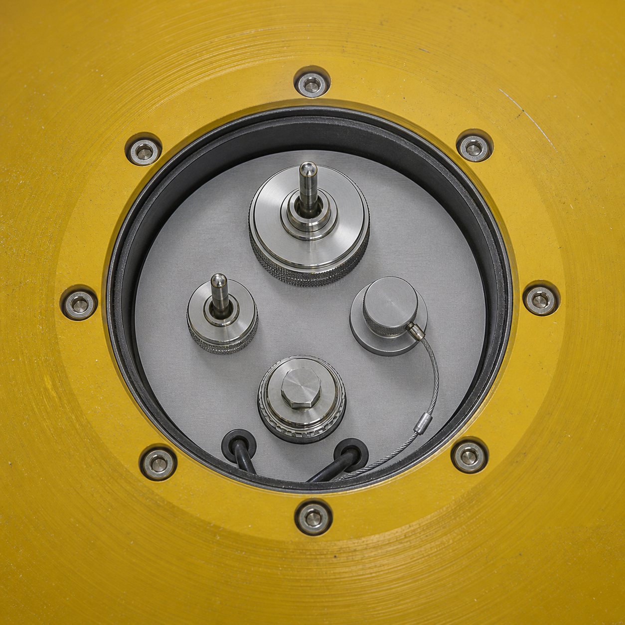 Top-down view of an open instrument hatch on a yellow buoy, with sealed stainless fittings and a bolted rim.